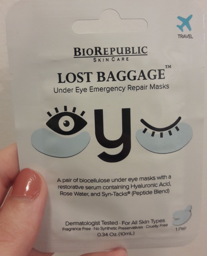 Image of the front packaging for BioRepublic's Lost Baggage Under Eye Emergency Repair masks. They show a stylized winking face wearing their masks. Their description: A pair of biocellulose under eye masks with a restorative serum containing Hylaluronic Acid, Rose Water, and Syn-Tacks (Peptide Blend)